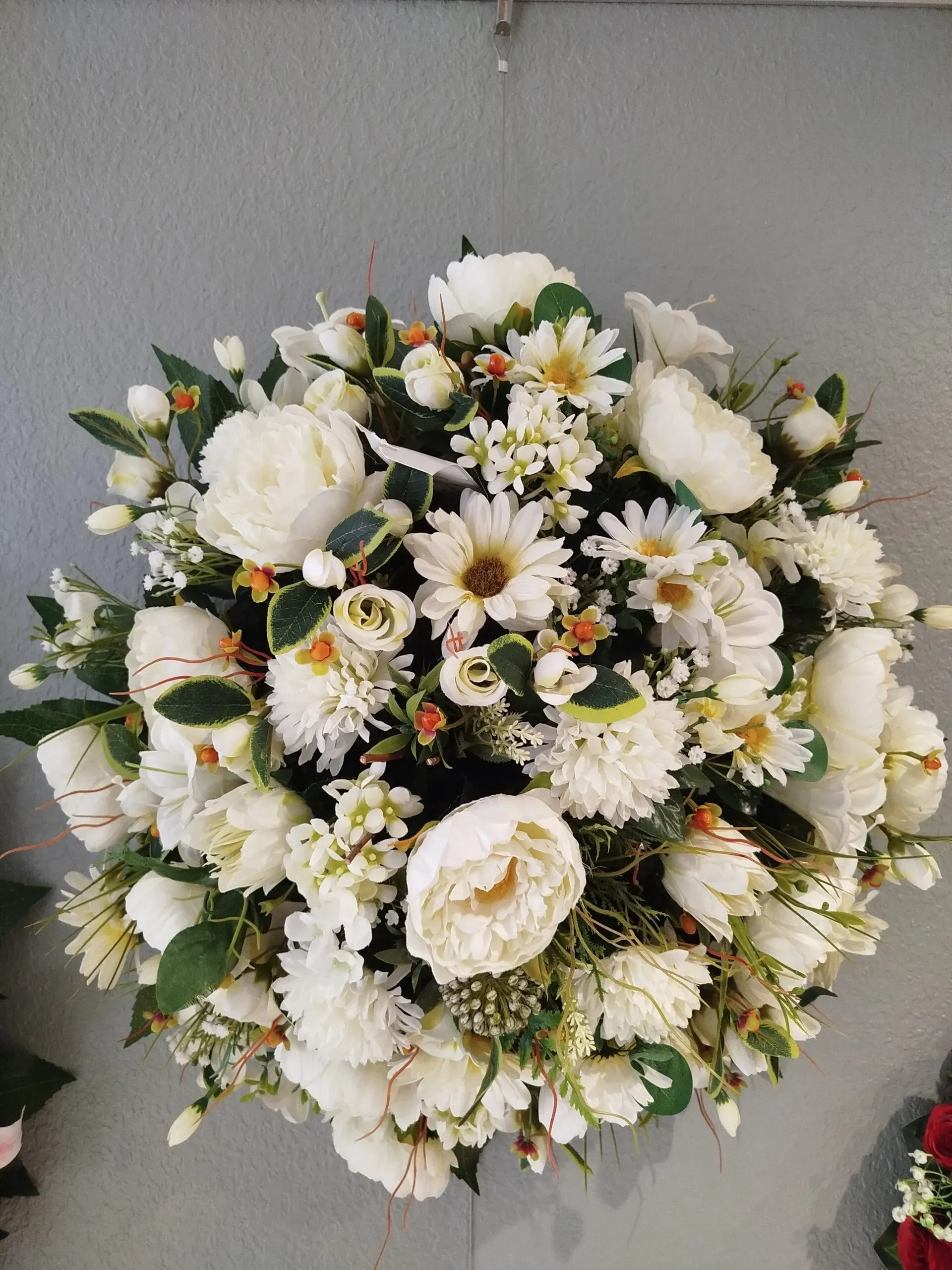 Balle de fleurs artificielles blanches, pivoines et marguerites sur mur gris.