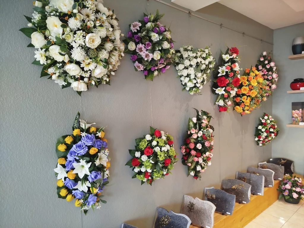 Mur gris décoré de nombreuses compositions de fleurs artificielles pour obsèques.
