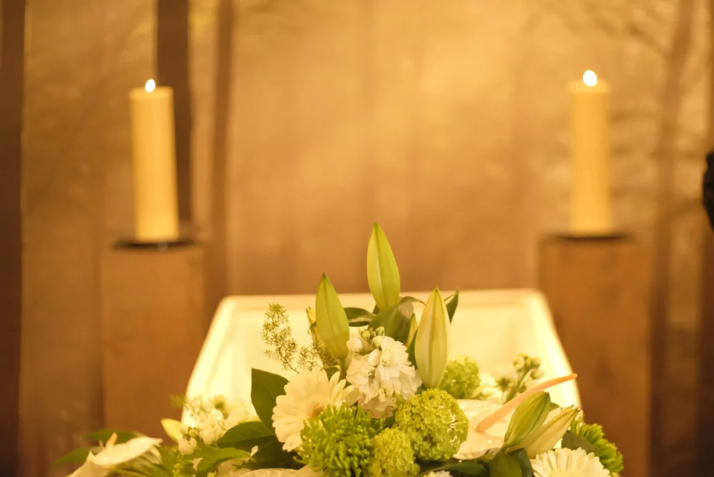 Arrangement floral funéraire blanc et vert devant des bougies allumées.